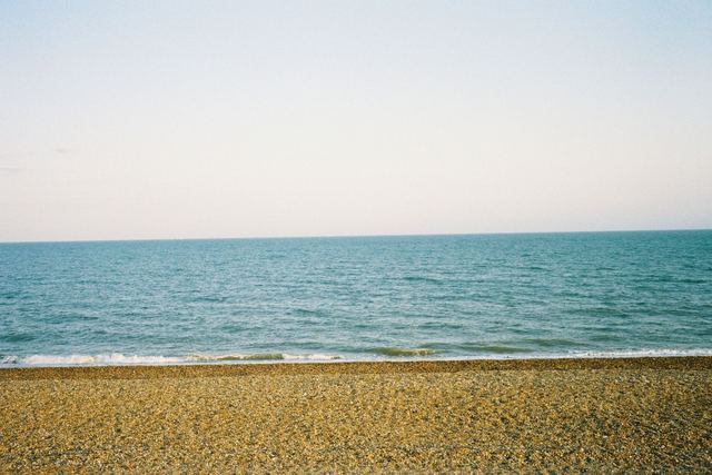 A shingle beach, a flat sea and a pale sky