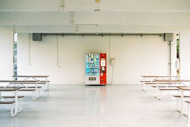 An empty white hall with benches and one red vending machine